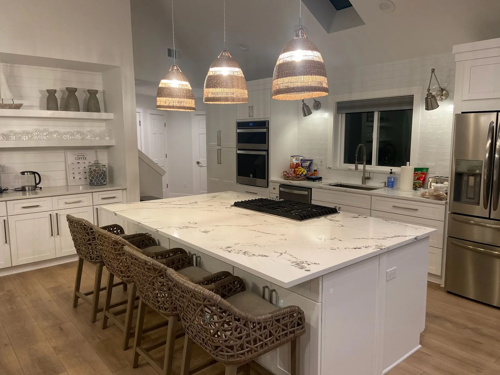 White kitchen with a veined island countertop and woven pendant lights