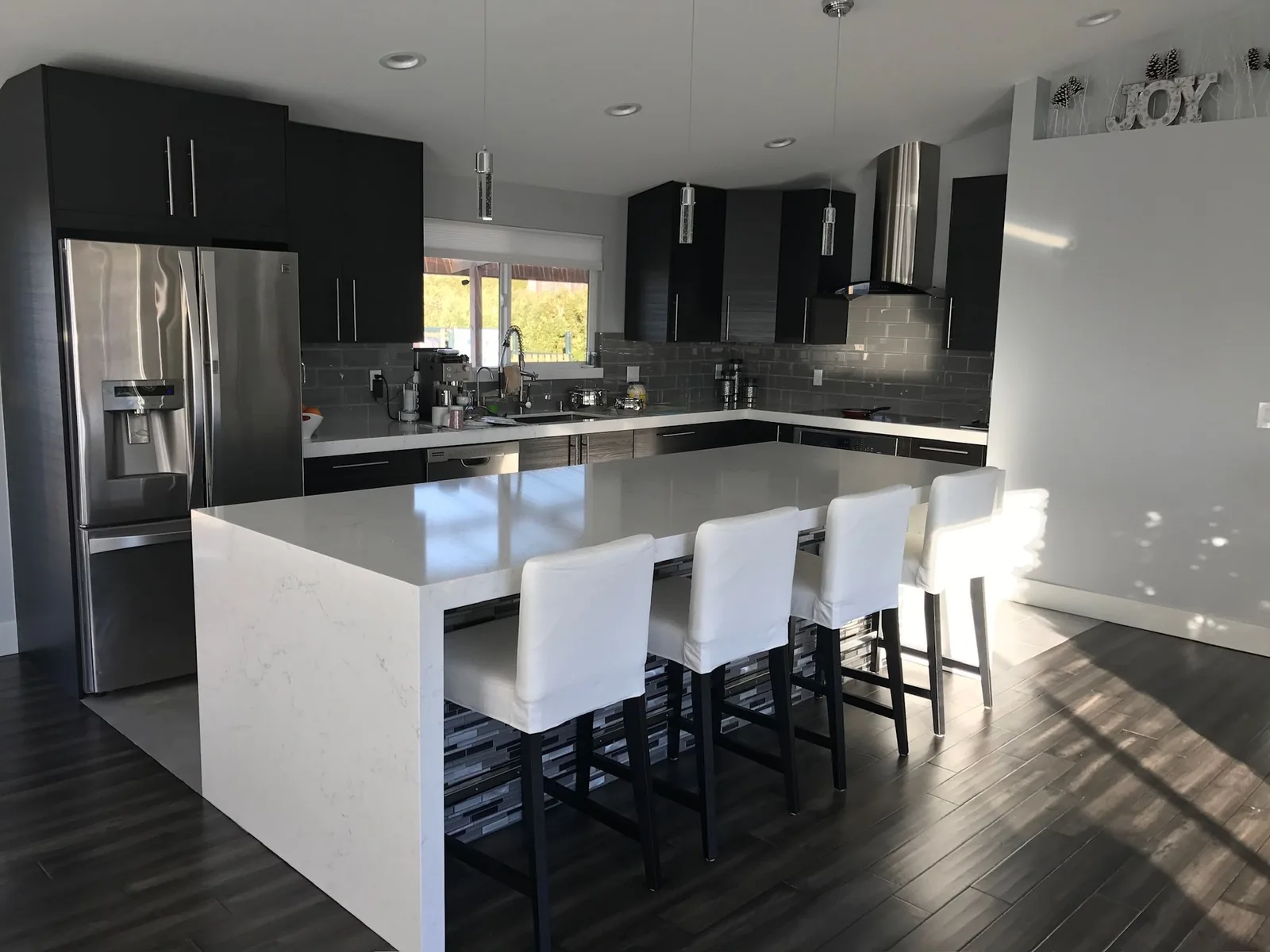 Black kitchen with a white waterfall island and white bar stools